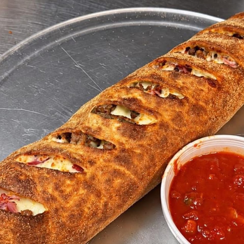 Golden-brown stuffed bread with visible cheese and meat filling, served alongside a bowl of red dipping sauce.