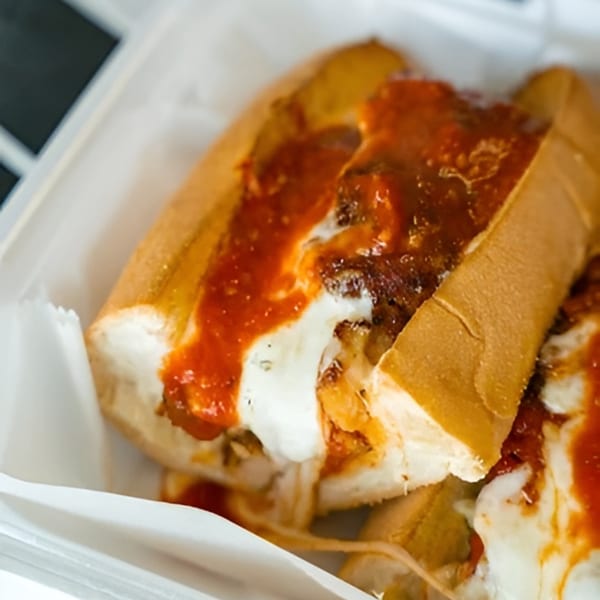 Meatball sub with melted mozzarella cheese and marinara sauce in a white takeout container.